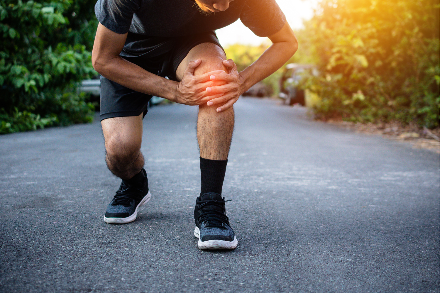 Runner grabbing knee in pain from iliotibial band syndrome during outdoor run